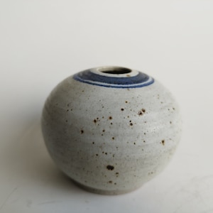 May include: A small, round, white ceramic vase with a blue and white stripe around the top.