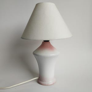 May include: White ceramic table lamp with a pink ombre base and a white fabric lampshade.