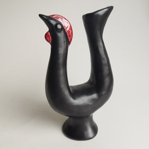 May include: Black ceramic rooster figurine with a red and white comb. The rooster is standing on a base with its legs raised in the air.