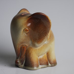 Könnte beinhalten: Eine Keramik-Elefantenfigur mit brauner Glasur an den Ohren und dem Rüssel. Der Körper ist hellbeige.