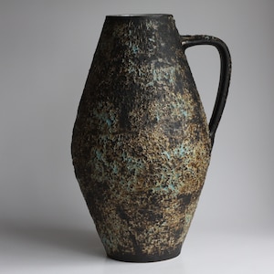 May include: A large, black ceramic vase with a textured surface and a light blue glaze. The vase has a wide mouth and a handle.