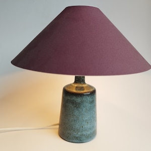 May include: A ceramic table lamp with a teal green base and a burgundy fabric lampshade.