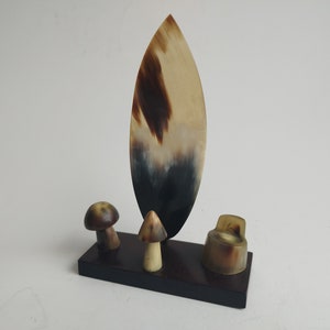 May include: A decorative horn sculpture with a brown and white pattern. The sculpture is shaped like a surfboard and is mounted on a black wooden base. There are three smaller horn sculptures on the base, shaped like mushrooms.