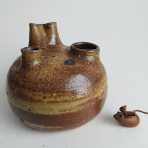 以下が含まれることがあります： 3つの開口部のある茶色とベージュの陶器の花瓶。花瓶は斑点と筋のある釉薬がかかっています。