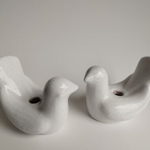 May include: Two white ceramic bird-shaped candle holders with a speckled finish. The holders have a small hole in the center for a candle.
