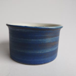 May include: A small, blue ceramic cup with a white interior. The cup has a striped pattern in shades of blue and brown.