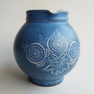 Peut inclure: Pichet en céramique bleu avec un corps rond et un bec verseur. Le pichet est orné d'un motif floral blanc. Le pichet mesure environ 18 cm de haut.