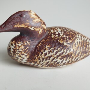 May include: A ceramic bird figurine with brown and white glaze. The bird is in a resting position with its head turned to the side.