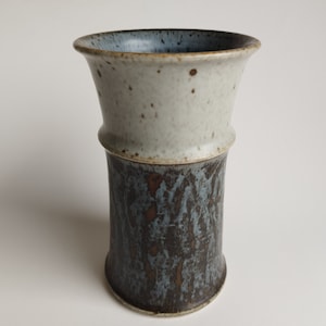 May include: A ceramic vase with a white and blue glaze. The vase has a wide mouth and a narrow base. It is a simple, elegant design.