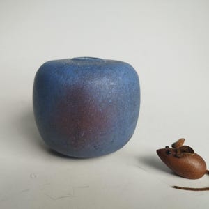 May include: A small, blue ceramic vase with a textured surface sits next to a brown leather mouse figurine.