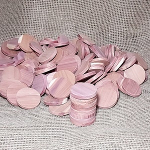 May include: A large pile of round, light pink cedar wood discs. The discs are stacked in a pile, with some of the discs standing upright. The discs are all about the same size and shape.