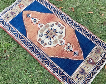 May include: A vintage rug with a blue, orange, and cream color scheme. The rug has a geometric pattern with a central diamond shape.
