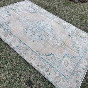 May include: A vintage rug with a light beige background and a teal blue floral pattern. The rug has a distressed look and is perfect for adding a touch of bohemian style to any room.
