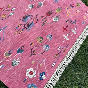 May include: A pink rug with a floral pattern in shades of blue, green, yellow, and red. The rug has a white fringe border.