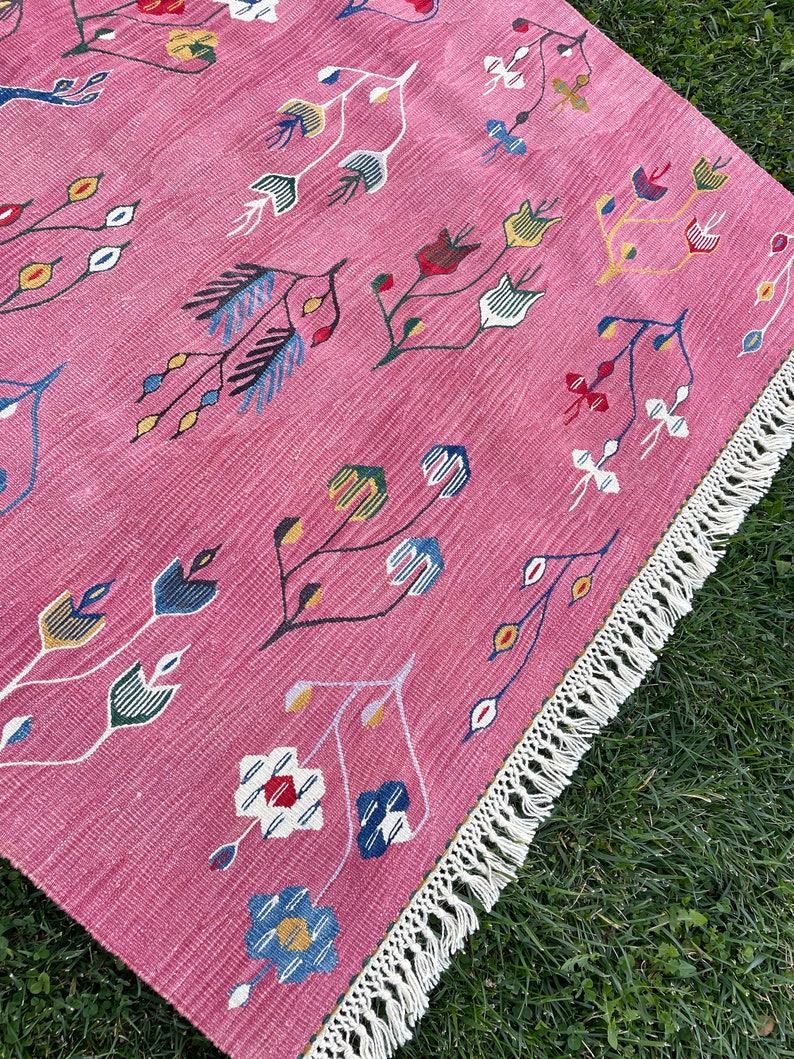 May include: A pink rug with a floral pattern in shades of blue, green, yellow, and red. The rug has a white fringe border.