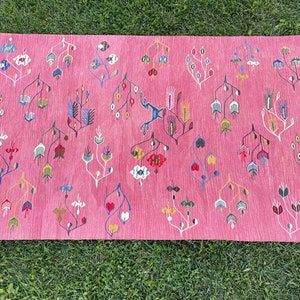May include: A pink rug with a floral pattern in shades of blue, red, yellow, and white. The rug has a fringe border.