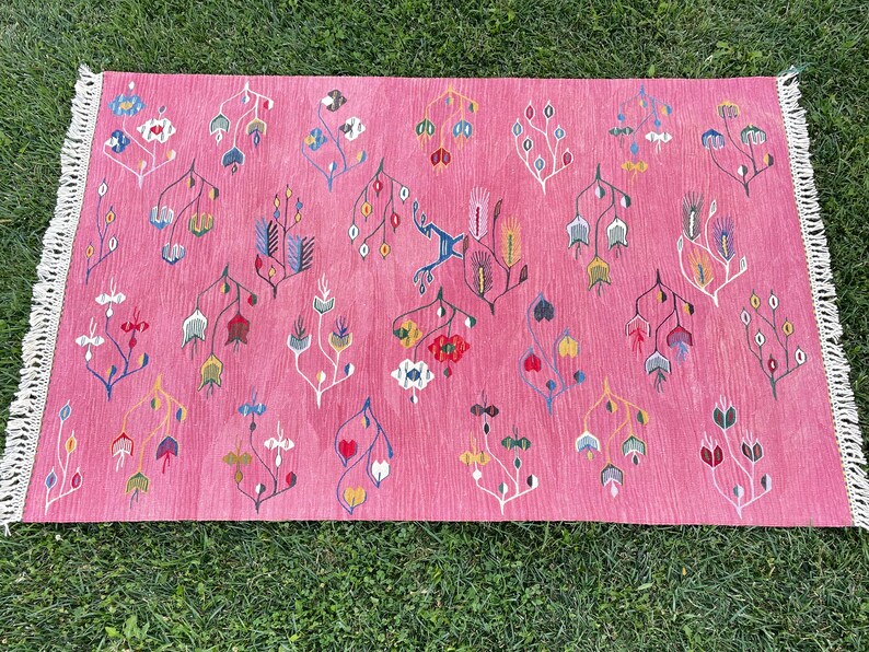 May include: A pink rug with a floral pattern in shades of blue, red, yellow, and white. The rug has a fringe border.