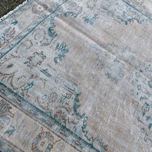 May include: A vintage rug with a faded beige background and a teal blue border. The rug has a traditional floral pattern.