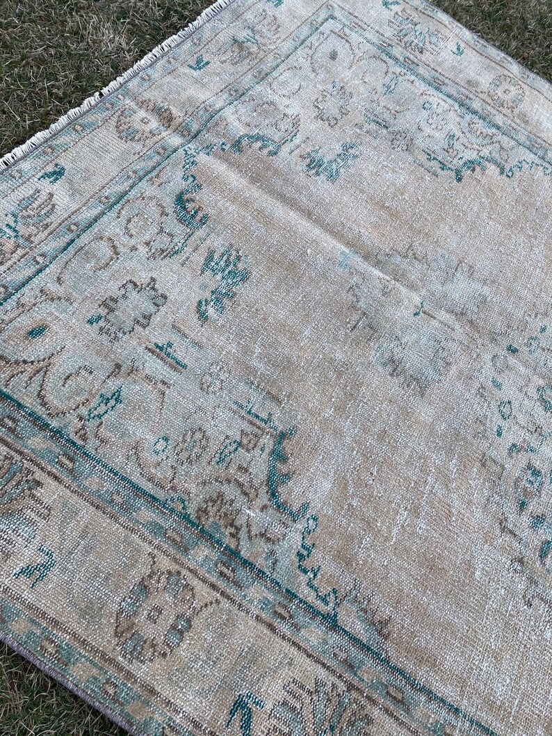May include: A vintage rug with a faded beige background and a teal blue border. The rug has a traditional floral pattern.