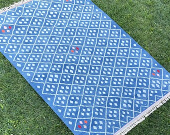 May include: A blue and white patterned rug with a diamond design. The rug has a fringe border and is made of a soft, woven material.