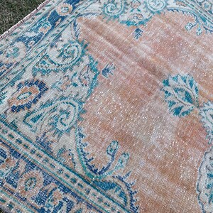 May include: A vintage rug with a faded peach background and a blue and teal floral pattern. The rug has a distressed look and is perfect for adding a touch of bohemian style to your home.