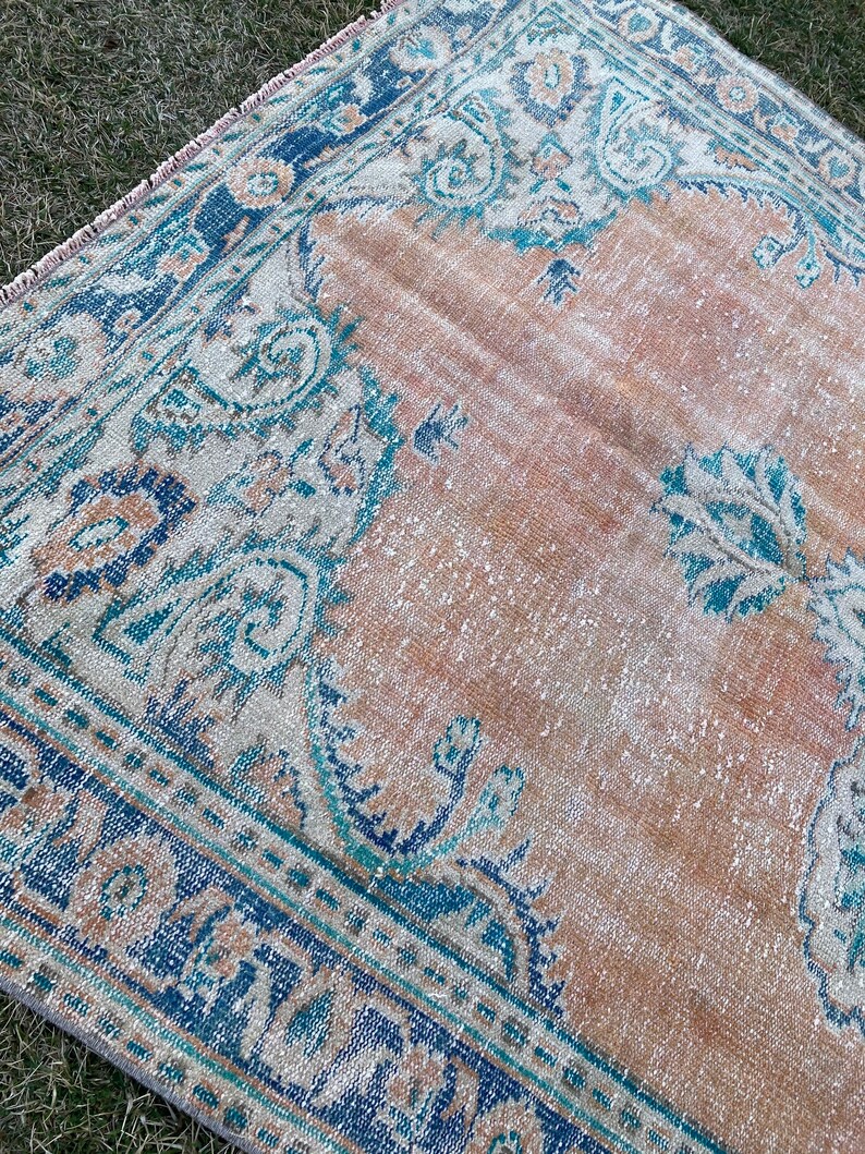 May include: A vintage rug with a faded peach background and a blue and teal floral pattern. The rug has a distressed look and is perfect for adding a touch of bohemian style to your home.