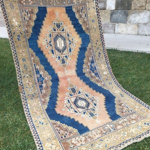 May include: A vintage rug with a blue and beige geometric pattern. The rug has a fringe border and is made of wool.
