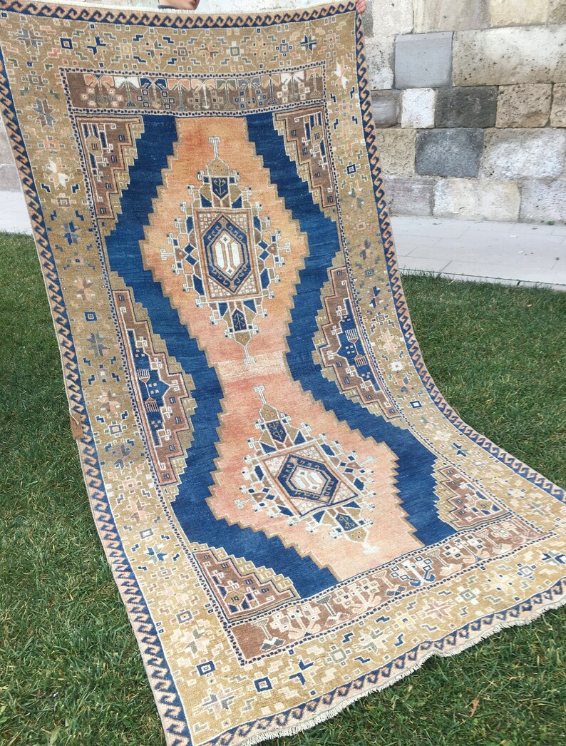 May include: A vintage rug with a blue and beige geometric pattern. The rug has a fringe border and is made of wool.