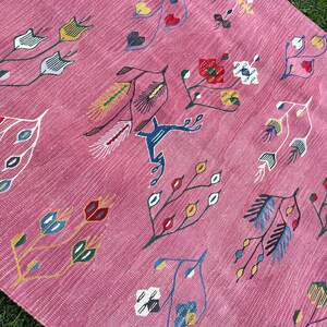 May include: Pink rug with a floral pattern. The rug features a variety of stylized flowers and leaves in shades of blue, red, yellow, and green.