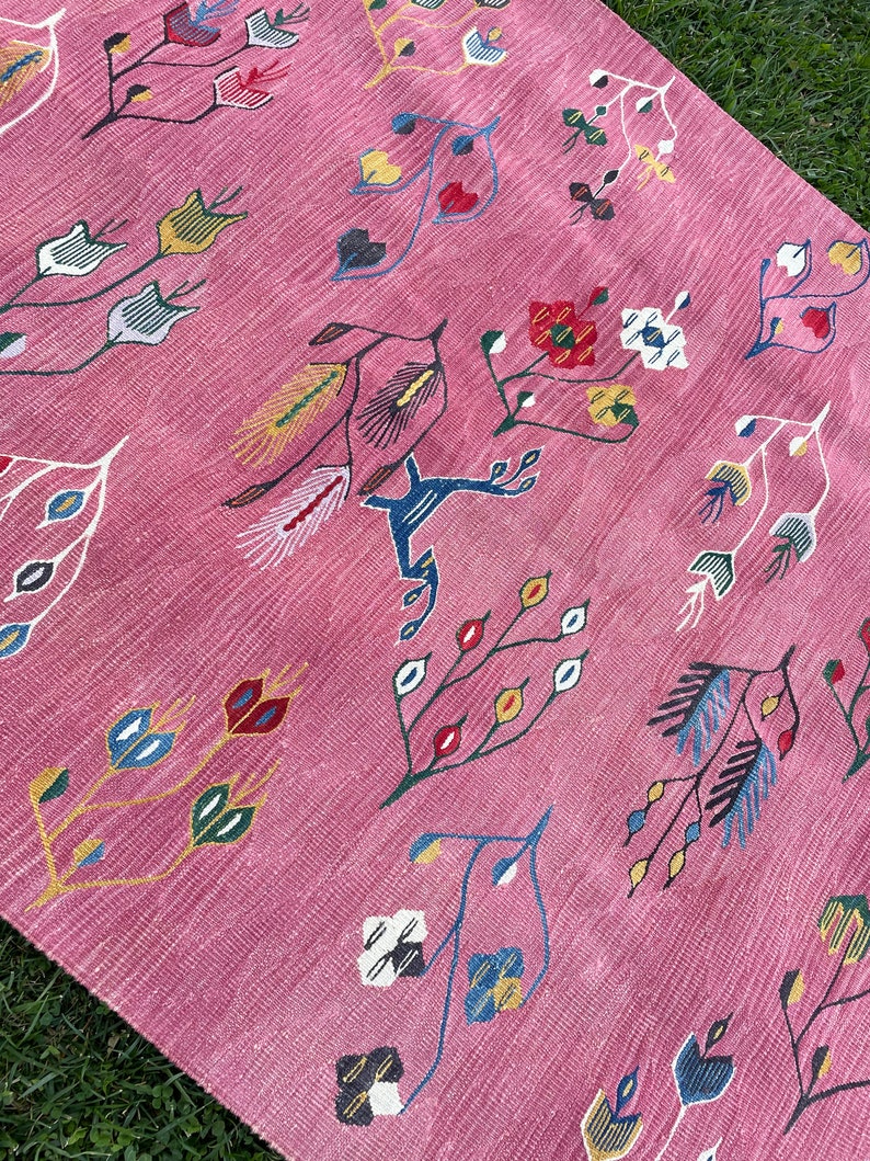May include: Pink rug with a floral pattern. The rug features a variety of stylized flowers and leaves in shades of blue, red, yellow, and green.