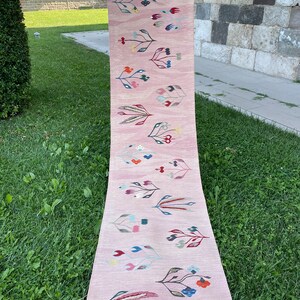 May include: A pink runner rug with a floral pattern in shades of red, blue, green, and yellow. The rug has a fringe border.