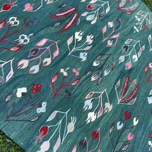 May include: A teal blue rug with a floral pattern in shades of pink, white, and red. The rug has a woven texture and a traditional design.