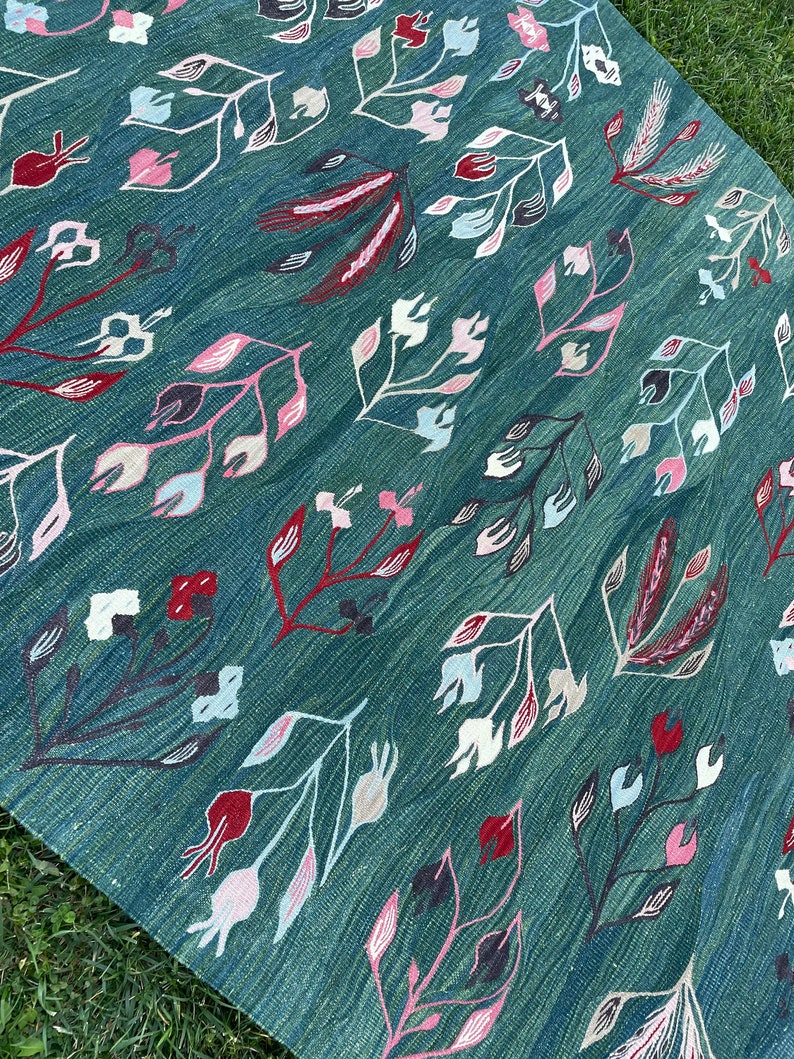 May include: A teal blue rug with a floral pattern in shades of pink, white, and red. The rug has a woven texture and a traditional design.