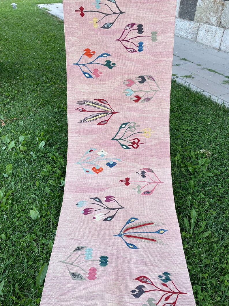 May include: A pink runner rug with a repeating pattern of stylized floral designs in shades of red, blue, green, yellow, and white.
