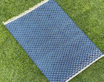 May include: A blue and white patterned rug with a fringe border. The rug has a geometric design with small white diamonds on a dark blue background.