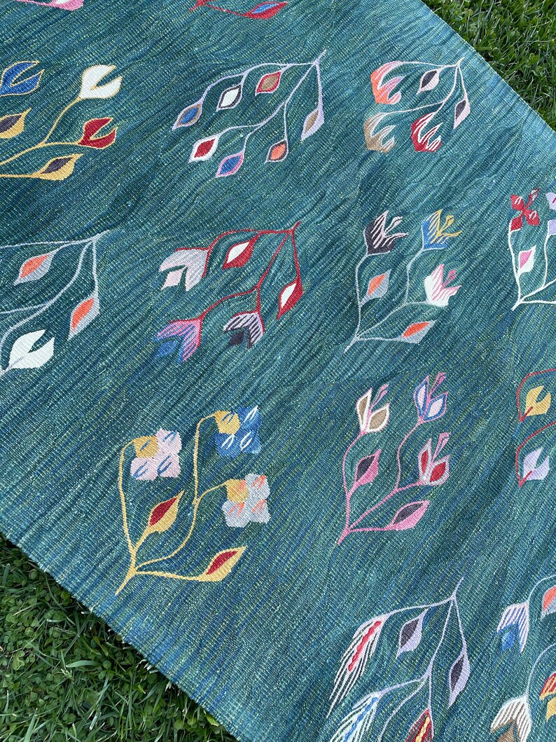 May include: A teal blue rug with a repeating pattern of stylized flowers in shades of pink, red, yellow, blue, and white.
