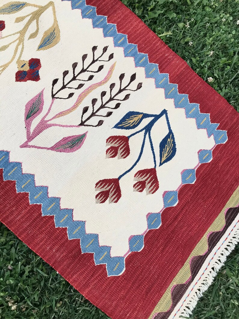 May include: A white and red rug with a floral pattern. The rug has a blue and white border and a fringe on the edges.
