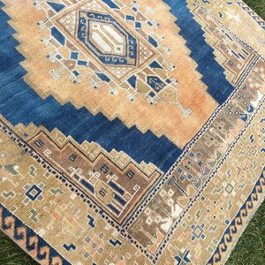 May include: A vintage rug with a blue and beige colour scheme. The rug has a geometric pattern with a central diamond shape. The rug has a fringed edge.