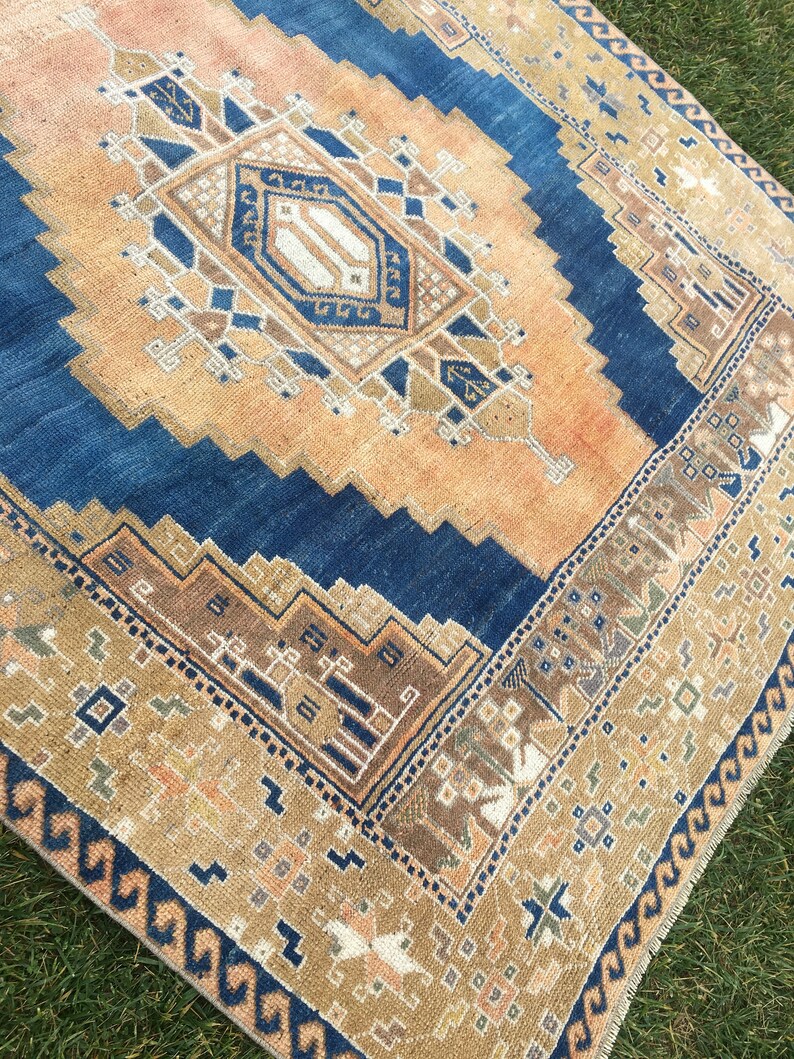 May include: A vintage rug with a blue and beige colour scheme. The rug has a geometric pattern with a central diamond shape. The rug has a fringed edge.