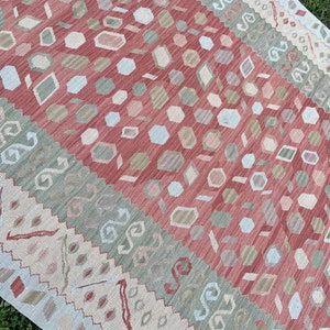 K&ouml;nnte beinhalten: Ein mehrfarbiger Teppich mit geometrischem Muster. Der Teppich hat ein rotes, gr&uuml;nes und wei&szlig;es Farbschema. Das Muster besteht aus kleinen, sich wiederholenden Formen.