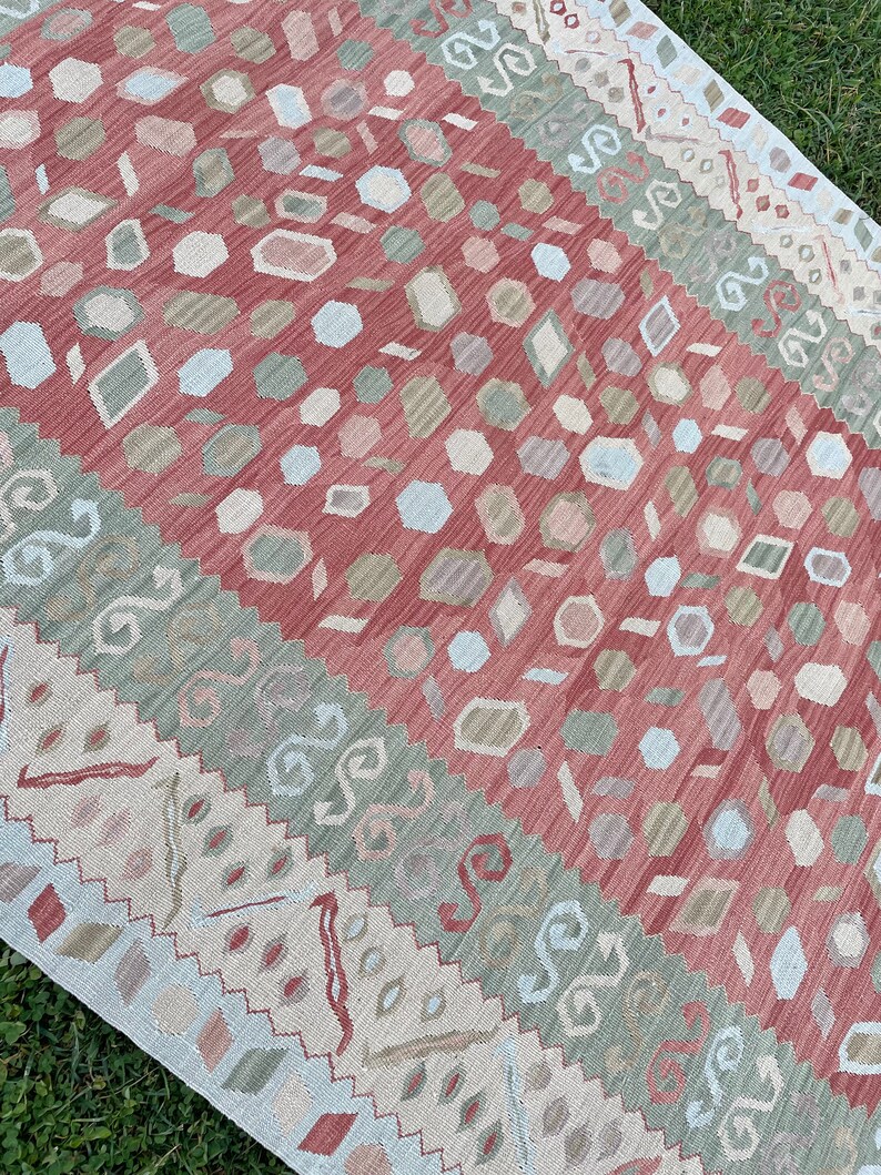 K&ouml;nnte beinhalten: Ein mehrfarbiger Teppich mit geometrischem Muster. Der Teppich hat ein rotes, gr&uuml;nes und wei&szlig;es Farbschema. Das Muster besteht aus kleinen, sich wiederholenden Formen.