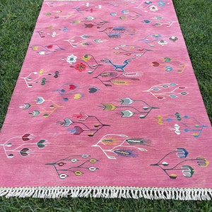 May include: A pink rug with a floral and geometric pattern. The rug has a white fringe border.