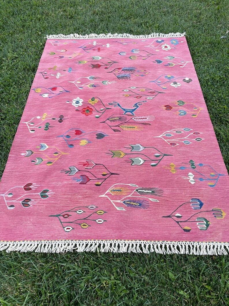 May include: A pink rug with a floral and geometric pattern. The rug has a white fringe border.