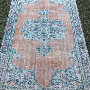 May include: A vintage rug with a faded peach background and a blue and teal floral pattern. The rug has a distressed look and a fringed edge.