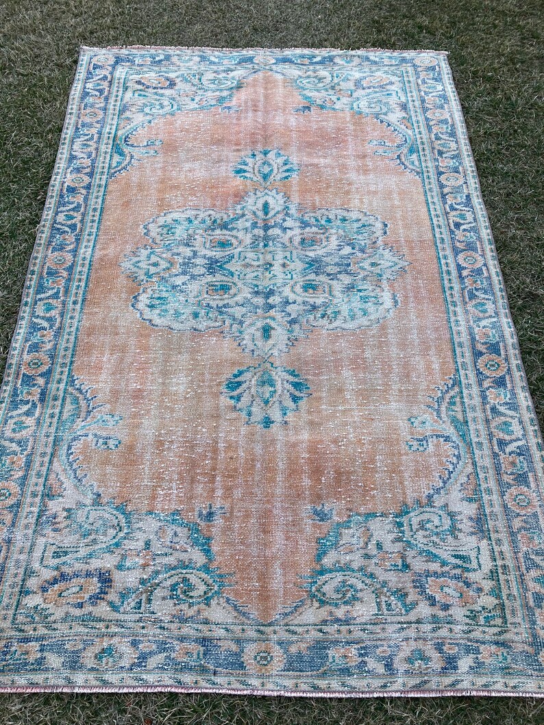 May include: A vintage rug with a faded peach background and a blue and teal floral pattern. The rug has a distressed look and a fringed edge.