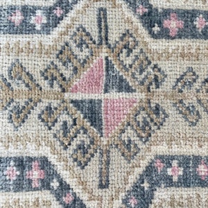 Puede incluir: Primer plano de una alfombra beige con un patr&oacute;n geom&eacute;trico en tonos grises y rosas. El patr&oacute;n presenta una forma de diamante con un diamante m&aacute;s peque&ntilde;o en su interior, rodeado por un borde de diamantes m&aacute;s peque&ntilde;os.