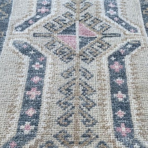 Puede incluir: Primer plano de una alfombra beige con un patr&oacute;n geom&eacute;trico en tonos grises y rosas. El patr&oacute;n presenta hojas y flores estilizadas.