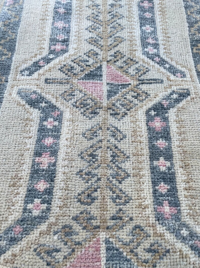 Puede incluir: Primer plano de una alfombra beige con un patr&oacute;n geom&eacute;trico en tonos grises y rosas. El patr&oacute;n presenta hojas y flores estilizadas.