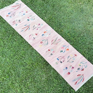 May include: A pink runner rug with a floral pattern in shades of blue, green, red, and yellow. The rug has a fringed edge.