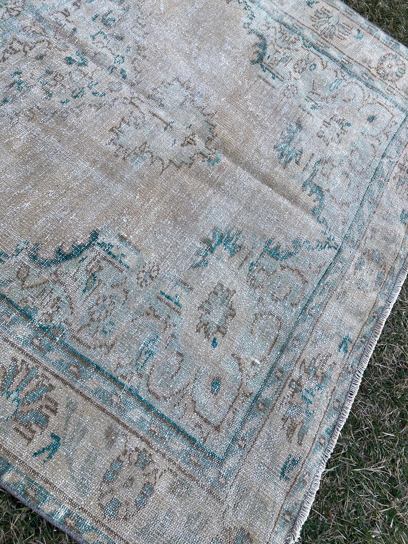 May include: A vintage rug with a faded light blue and brown pattern. The rug has a distressed look and is made of a soft, woven material.